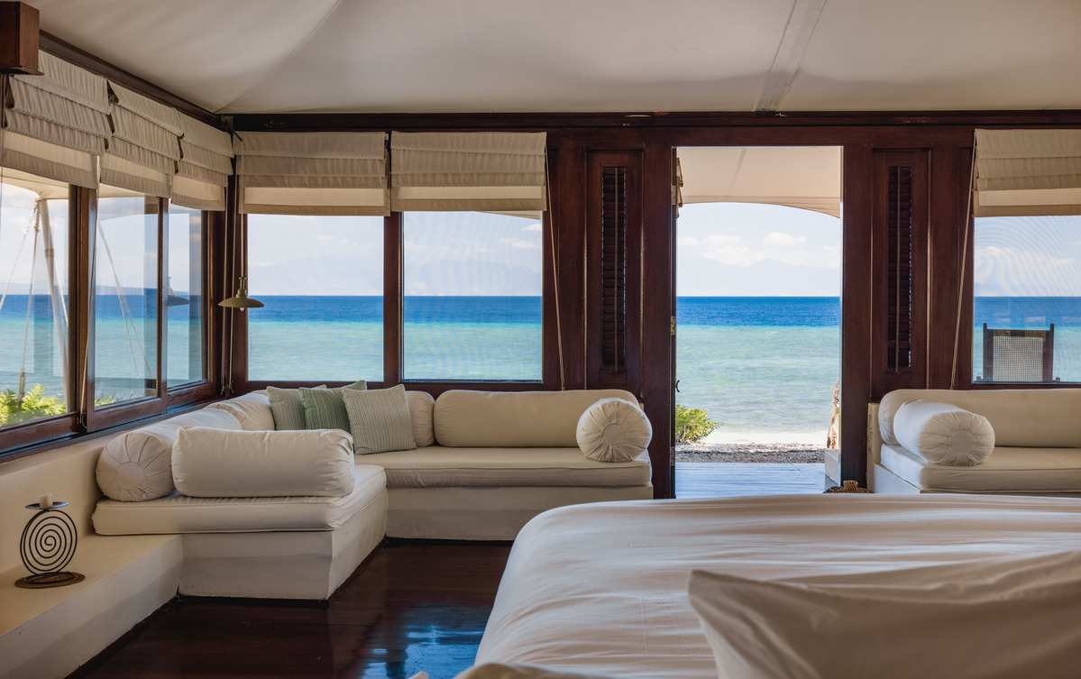 Interior of a bedroom at Amanwana showing a white sofa and bed with a direct view of the blue sea.