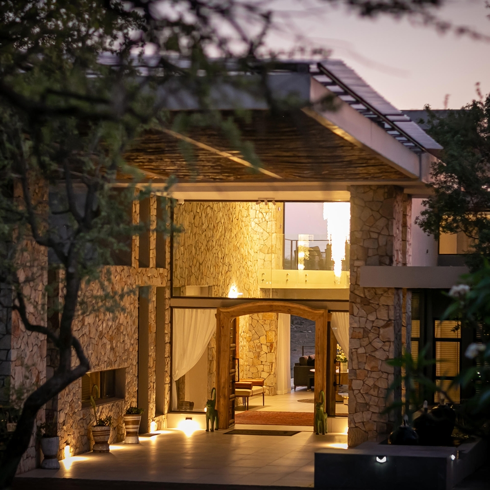 Illuminated modern house with stone walls and warm interior lights at dusk.