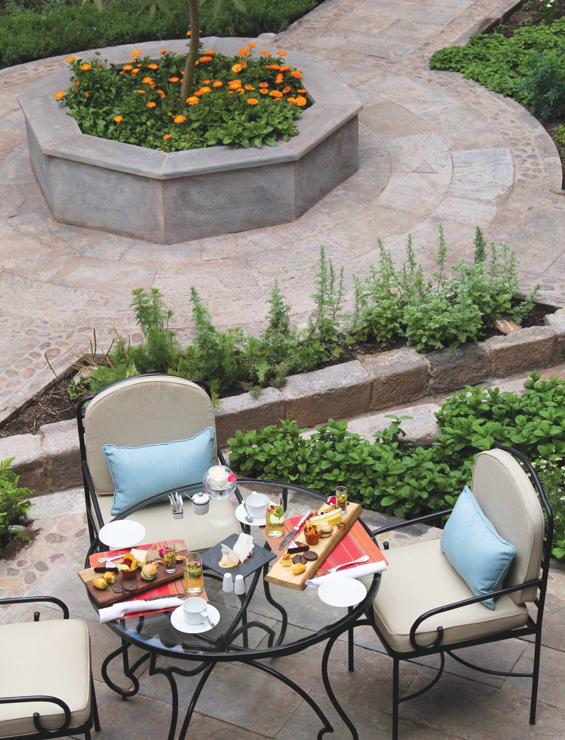 Outdoor patio table with breakfast setup, overlooking a landscaped area with flowers.