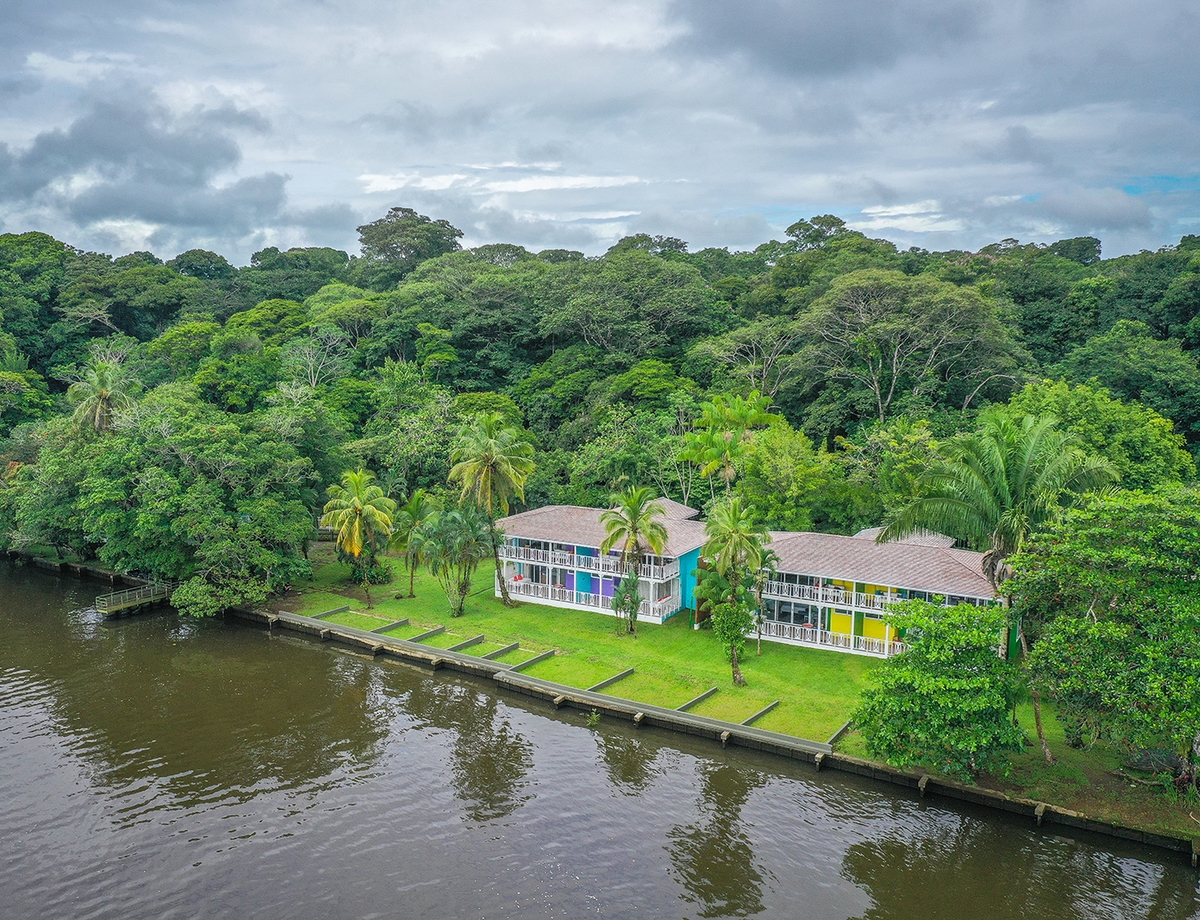 Colorful two-story lodge buildings on a green lawn beside a wide river at Tortuga Lodge Costa Rica.