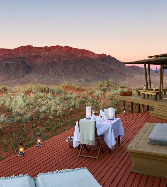 Private dinner table set on a wooden deck with lanterns and a mountain backdrop at twilight.