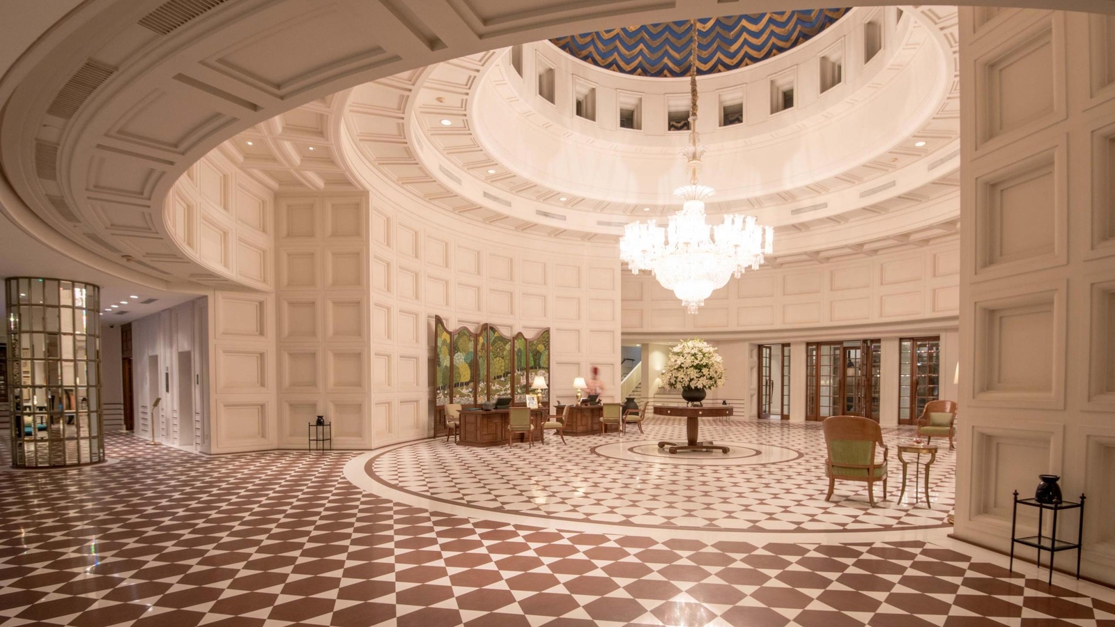 Large circular hotel lobby with a crystal chandelier, checkered marble floor, and a grand domed ceiling.