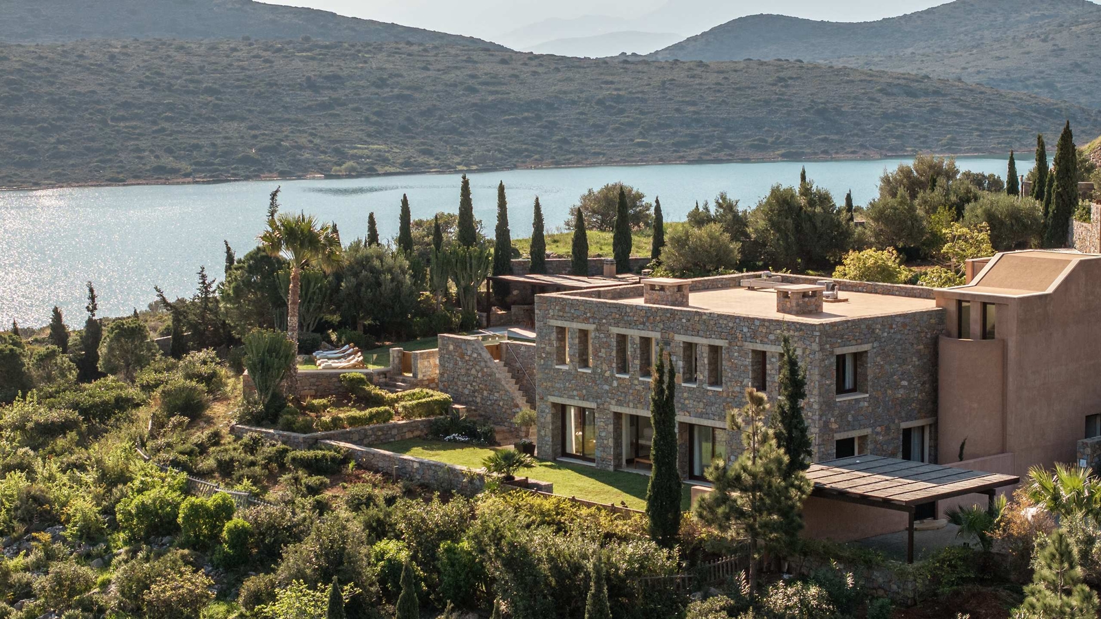 Aerial view of a villa at Phaea Blue Palace in Crete with surrounding trees and water in the background