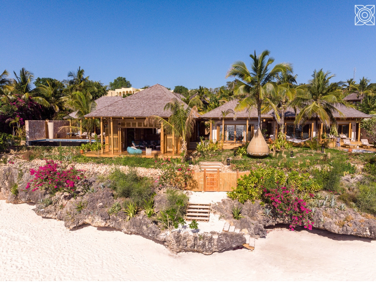 Tropical wooden villas with thatched roofs located on a cliffside above a white sand beach at Zuri Zanzibar.