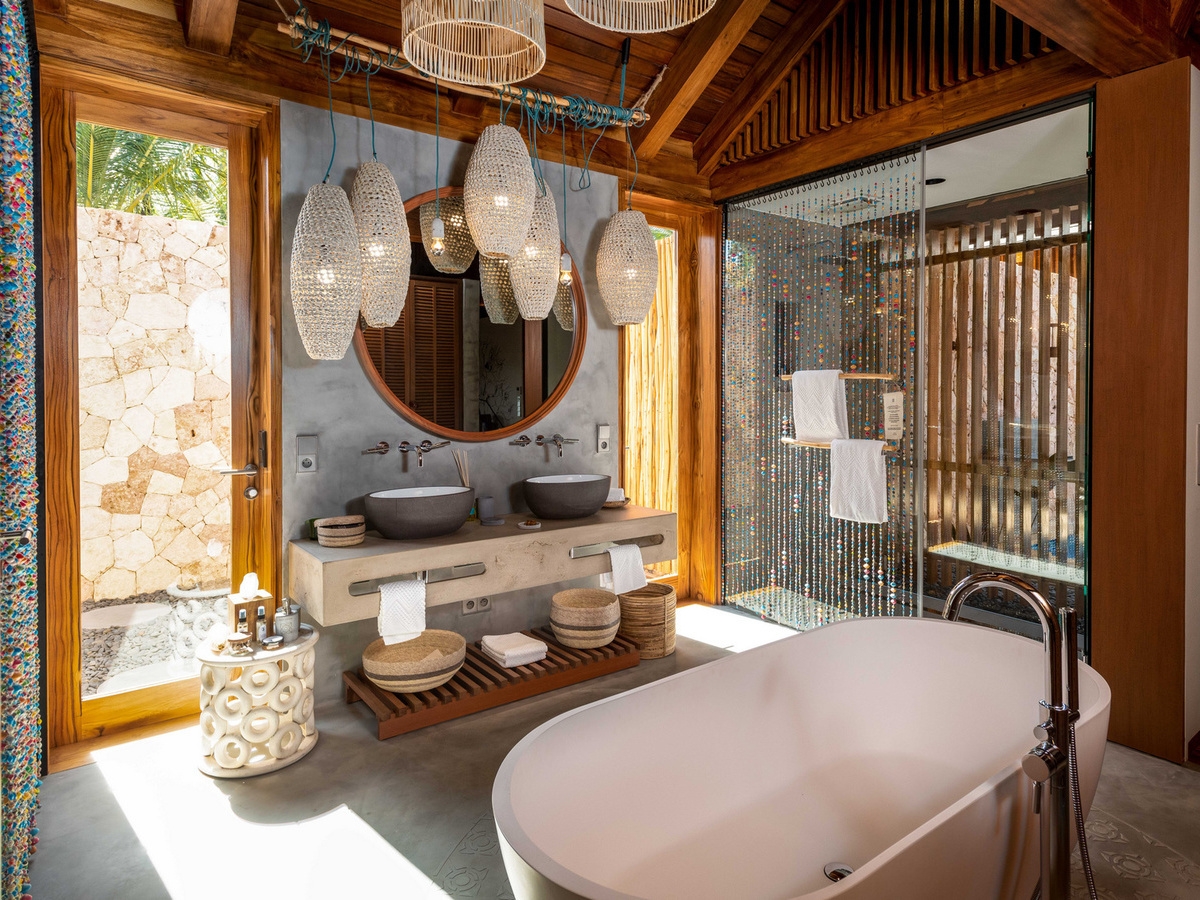 Modern bathroom with a large oval soaking tub, wooden accents, and woven pendant lights at Zuri Zanzibar.