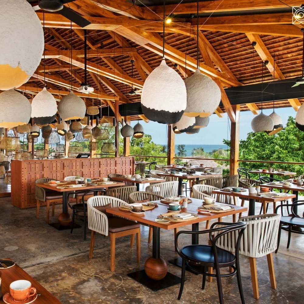 Indoor-outdoor restaurant with wooden beams, unique white and black pendant lamps, and ocean views at Zuri Zanzibar.
