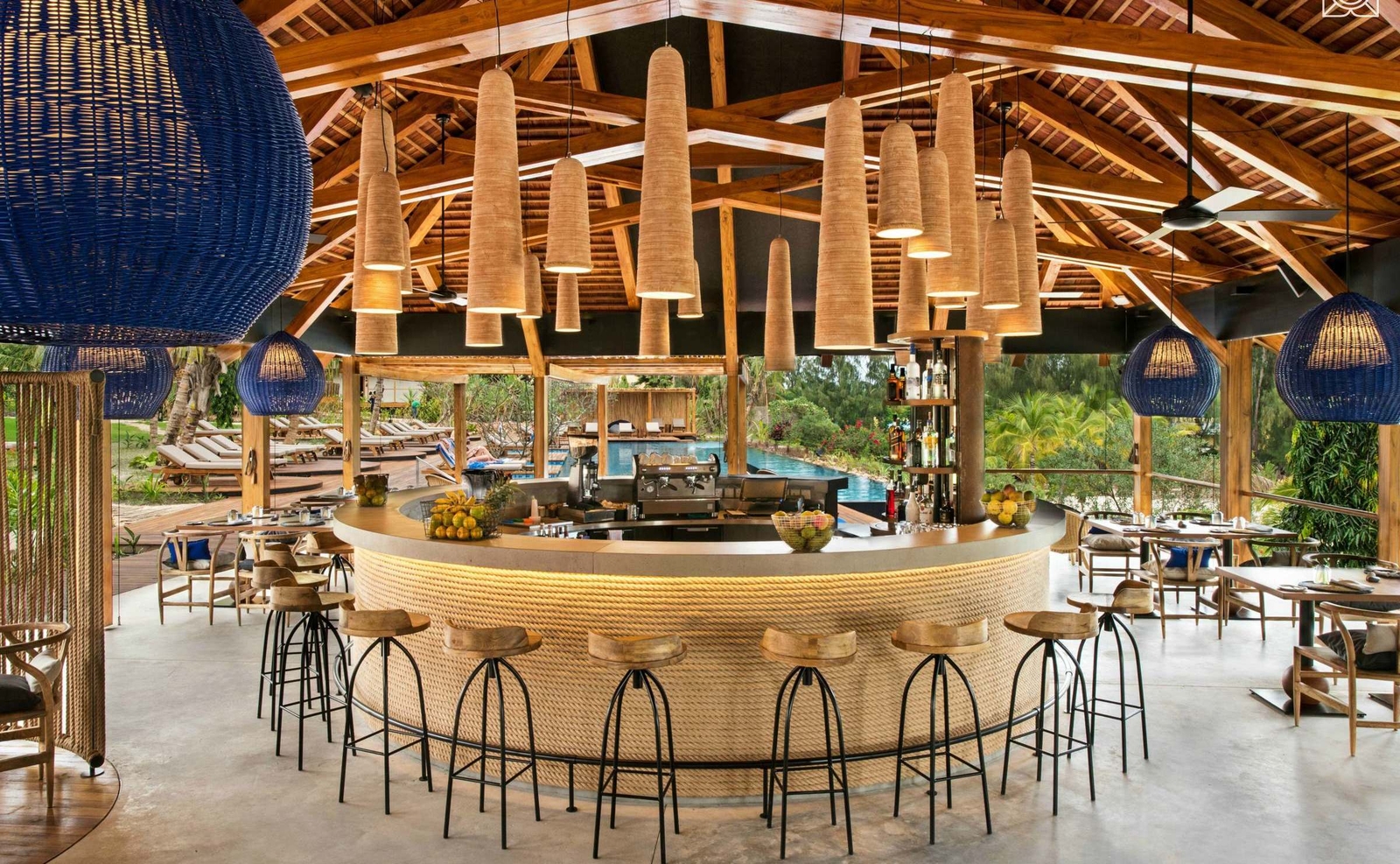 Circular poolside bar with rope detailing, wooden bar stools, and many hanging neutral-toned lamps at Zuri Zanzibar.