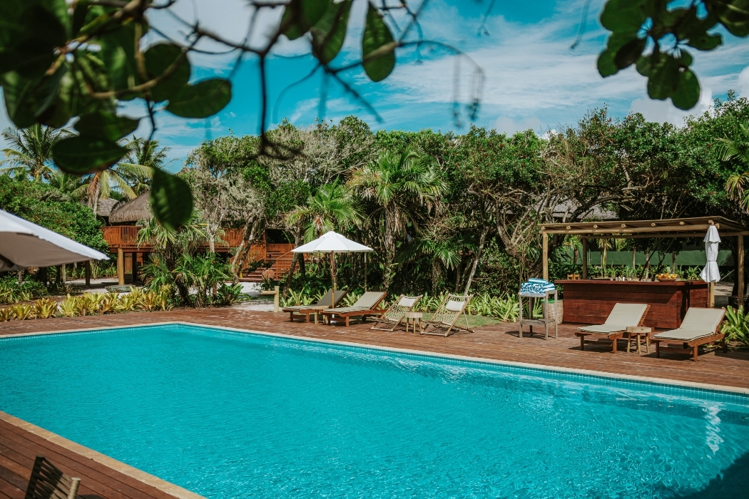 A tropical resort pool with sun loungers, umbrellas, and a bar surrounded by lush greenery.