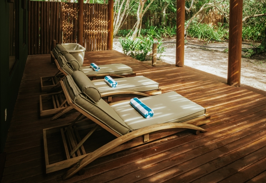 Three wooden sun loungers with towels on a tranquil patio amidst tropical greenery.