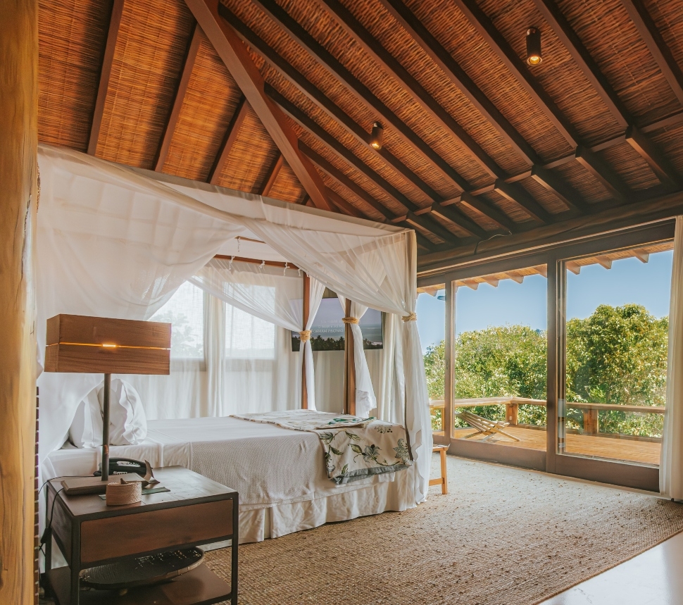 A cozy bedroom with a canopy bed, wooden ceilings, and a view of greenery outside.