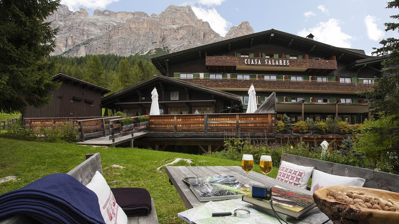 Exterior of Ciasa Salares, garden table with drinks and strewn with maps, Italy