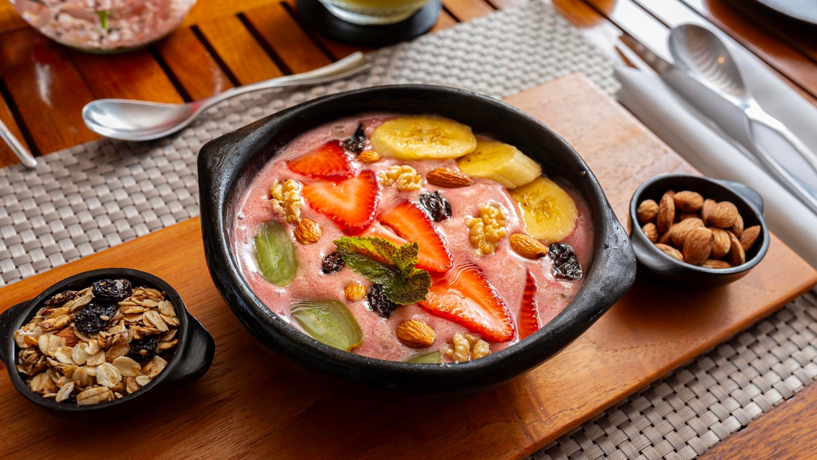 A bowl of acai smoothie topped with sliced fruits, nuts, and granola on a wooden table.