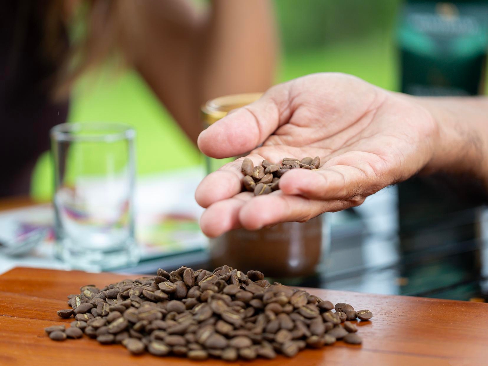A hand holding coffee beans over a pile on a wooden table, with a blurred background.