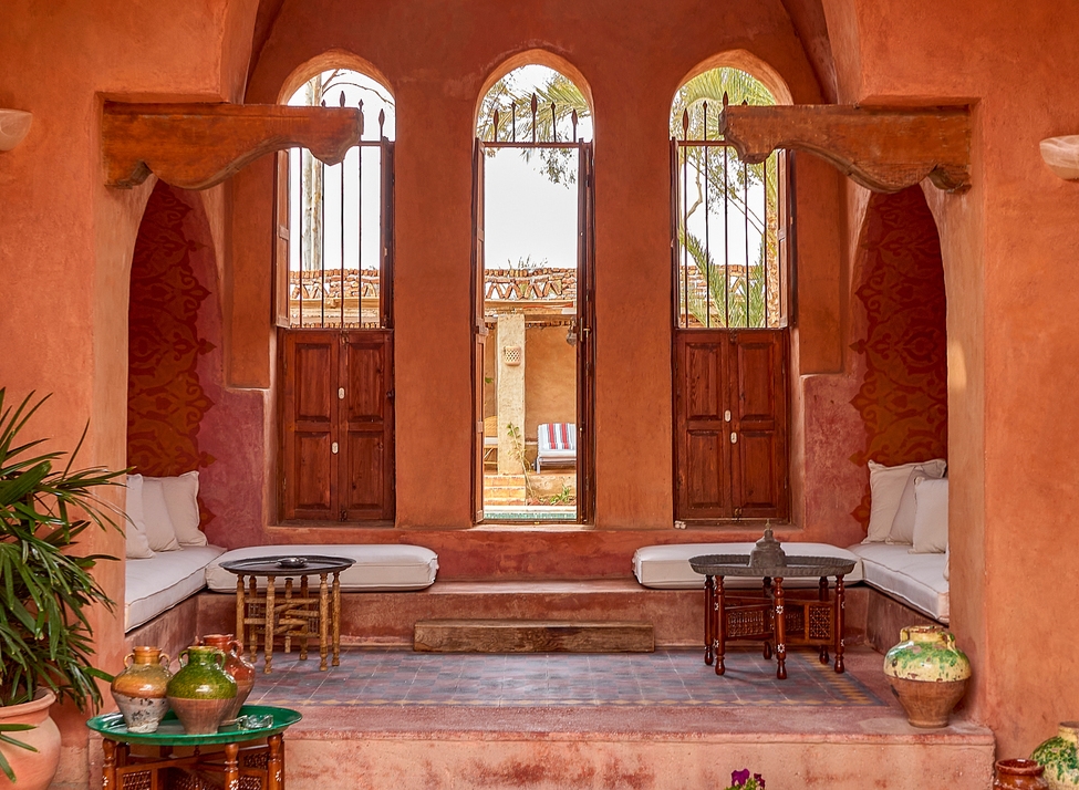 A terracotta-walled courtyard with three arched windows, low cushioned seating, and decorative pottery at Al Moudira Luxor.