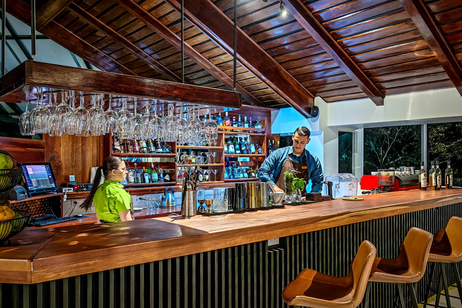 Staff working behind a well-stocked wooden bar with hanging glassware at Monteverde Lodge.
