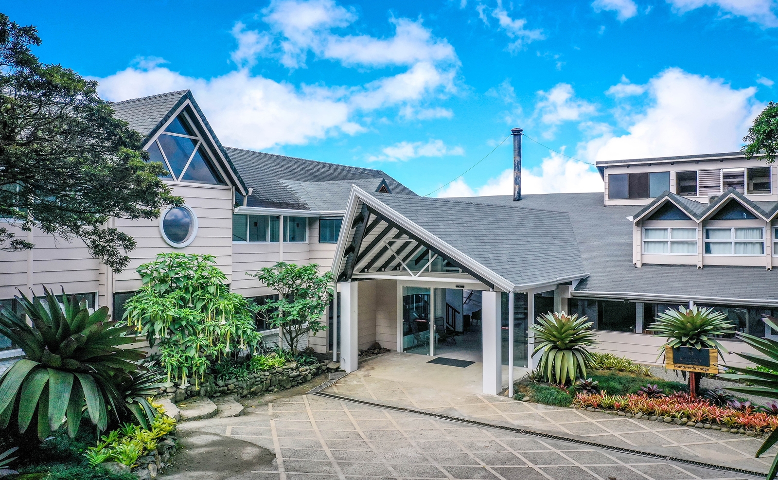 Exterior of Monteverde Lodge showing the white gabled entrance, stone pathways, and tropical plants.