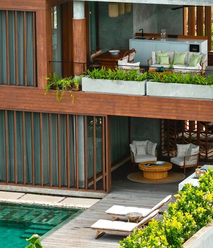 Exterior of a two-story wood-clad villa at Cap Karoso with a private pool, lounge chairs, and balcony seating areas.