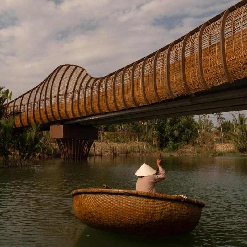 A person in a traditional basket boat paddling under a bamboo bridge at Namia River Retreat.