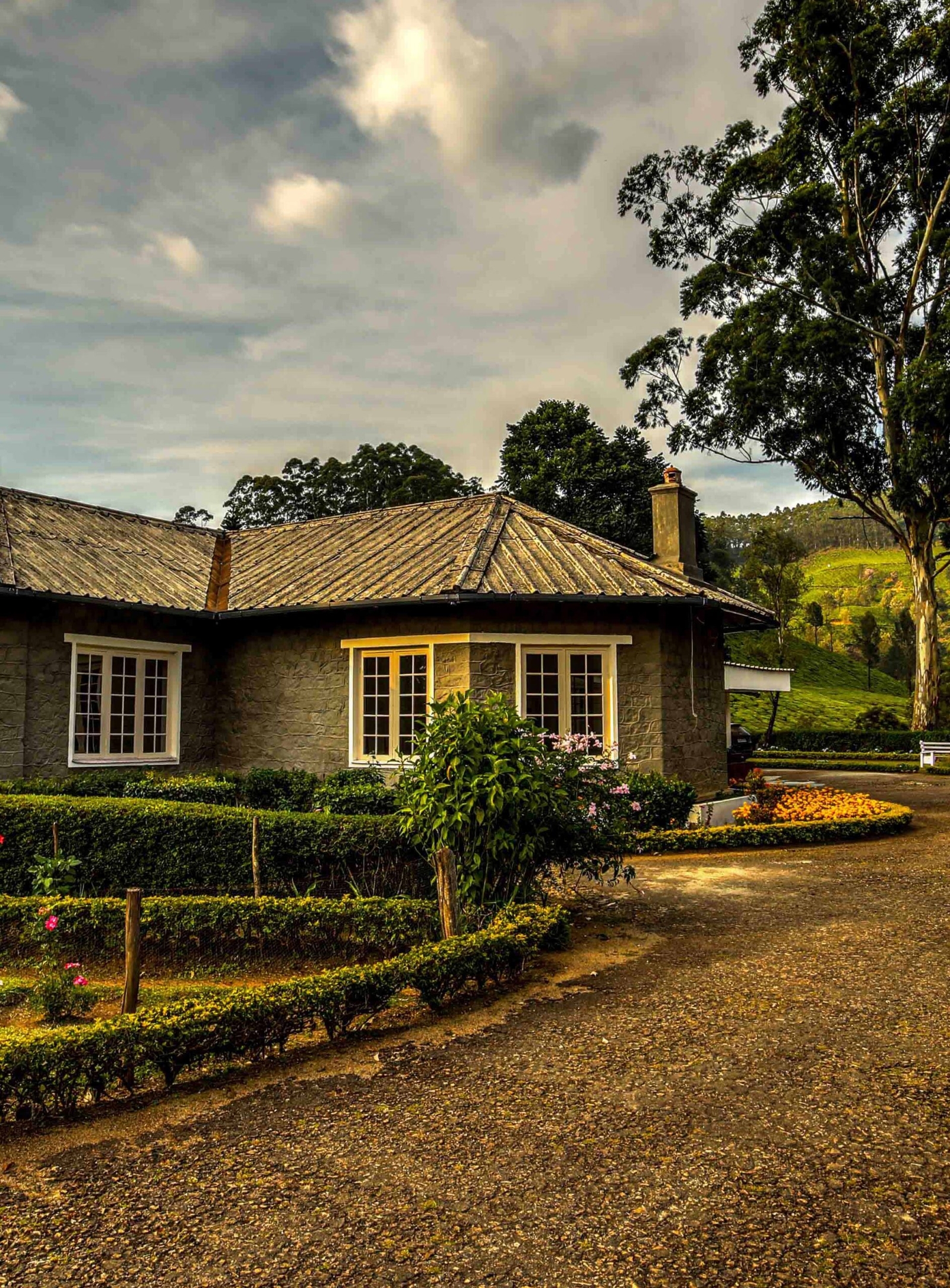 A quaint stone cottage with landscaped garden and cloudy skies.
