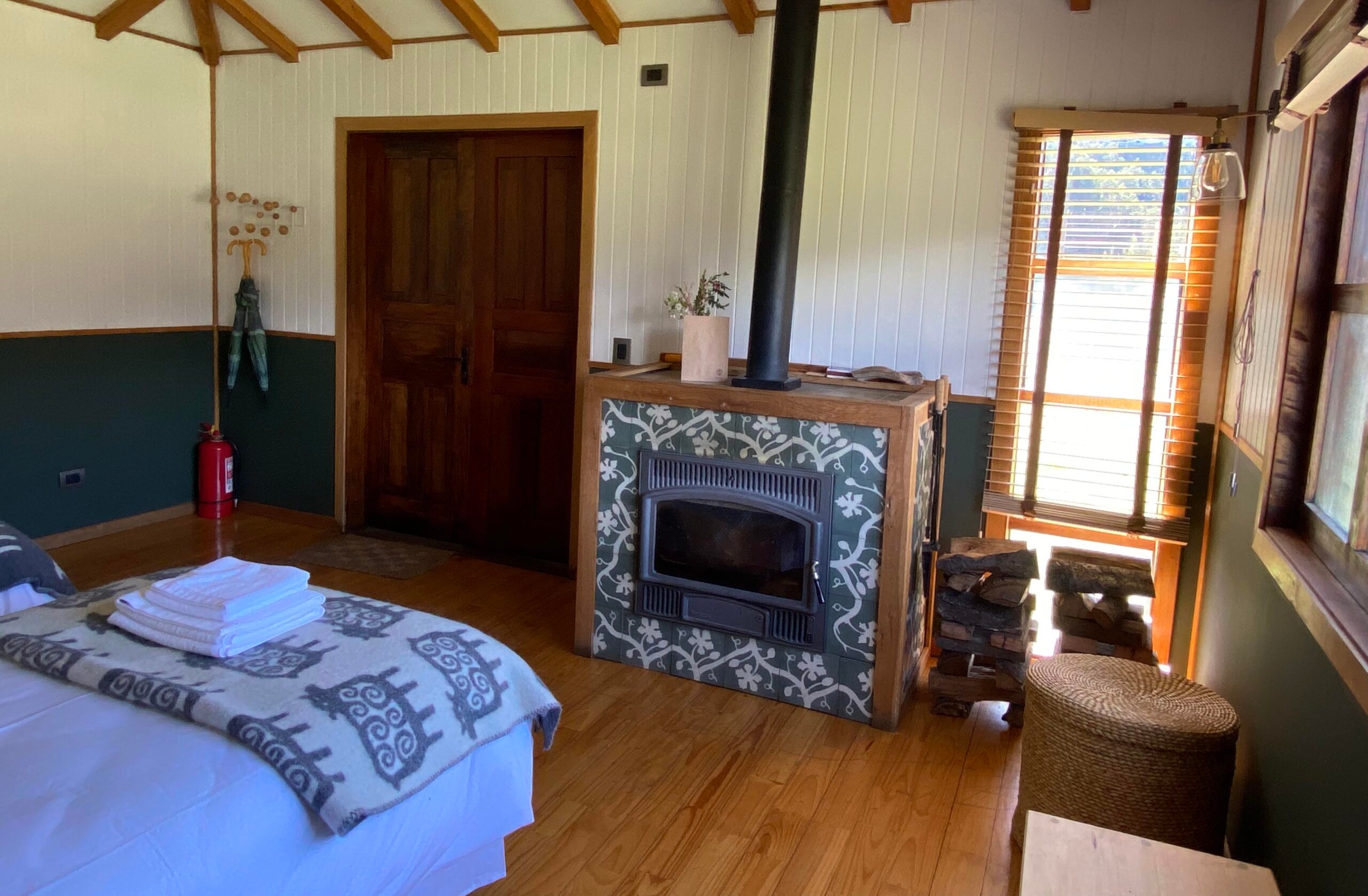 A cozy cabin room with a bed, fireplace, wood logs, and a window with blinds.