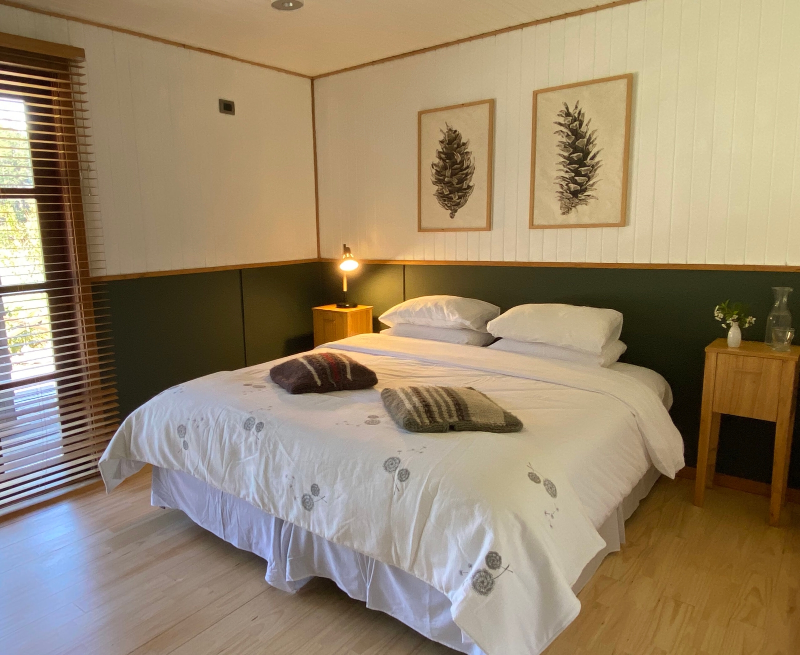 A cozy bedroom with a double bed, white bedding, wooden walls, and botanical art.