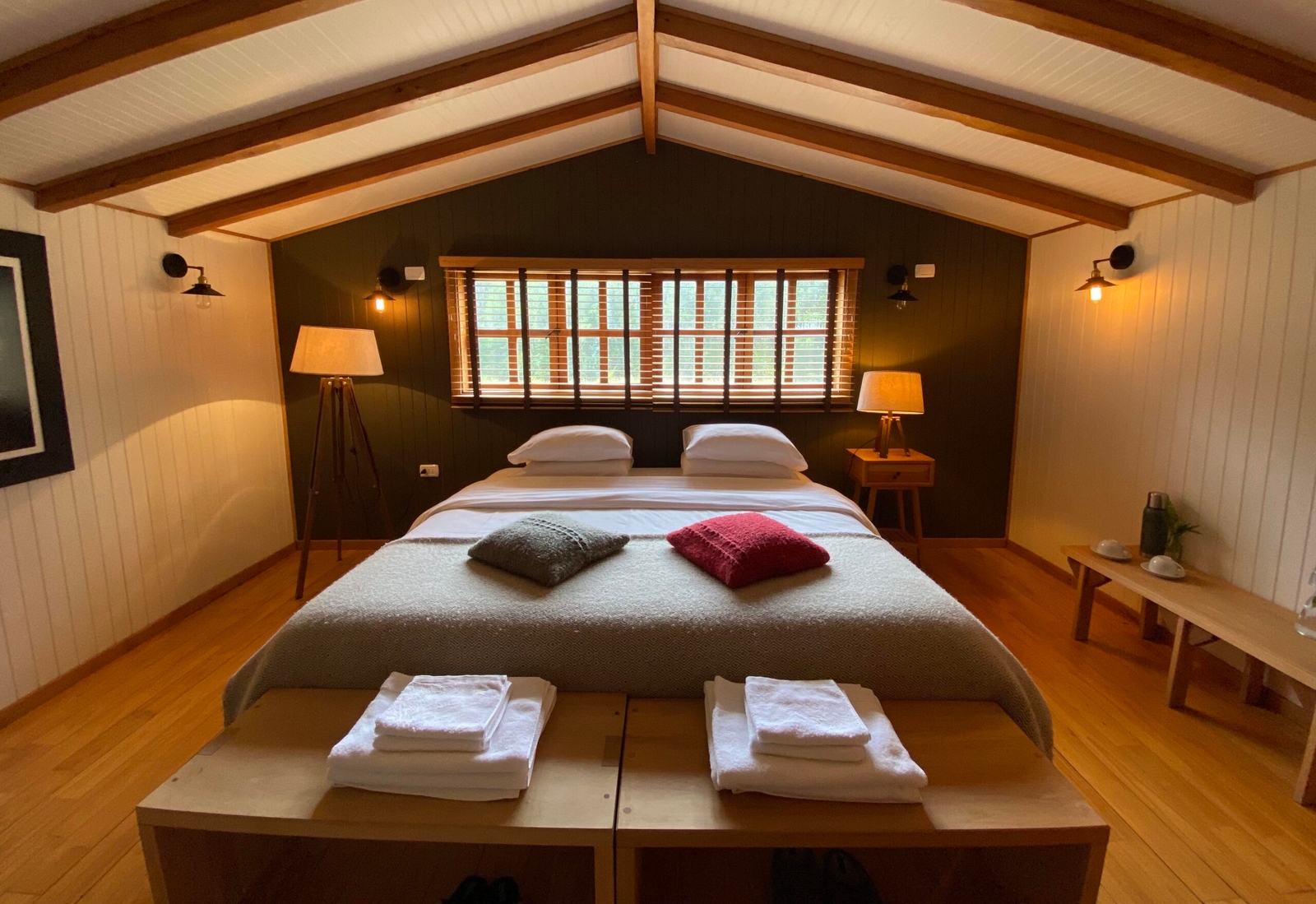 Cozy bedroom with a large bed, wooden accents, warm lighting, and two windows.