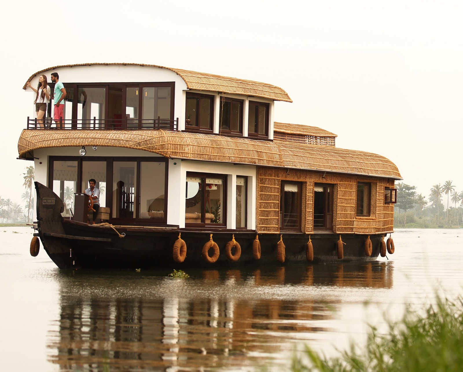 A traditional houseboat with thatched roof on calm waters surrounded by palm trees.