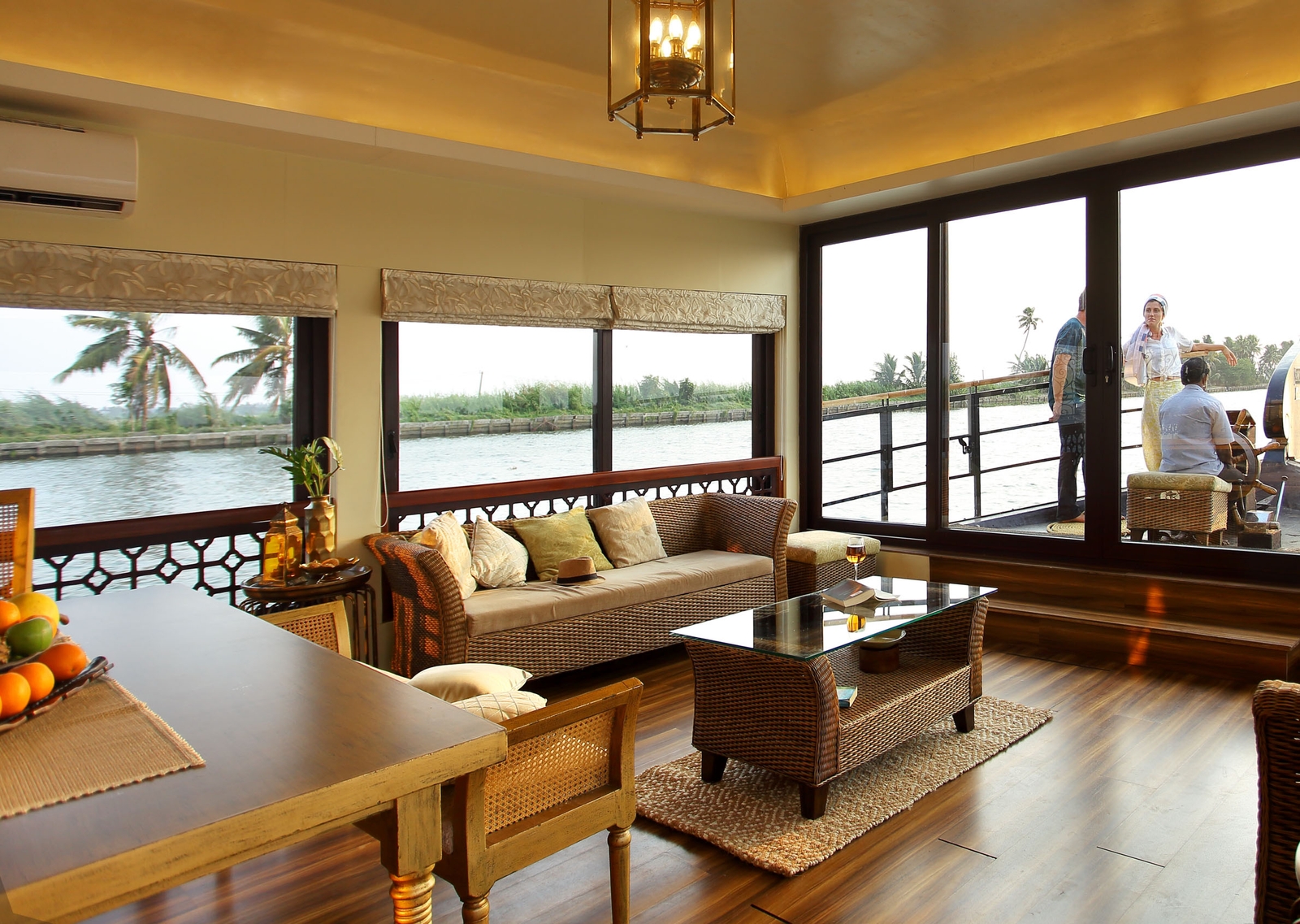 A cozy living room with wicker furniture overlooking a riverside balcony.