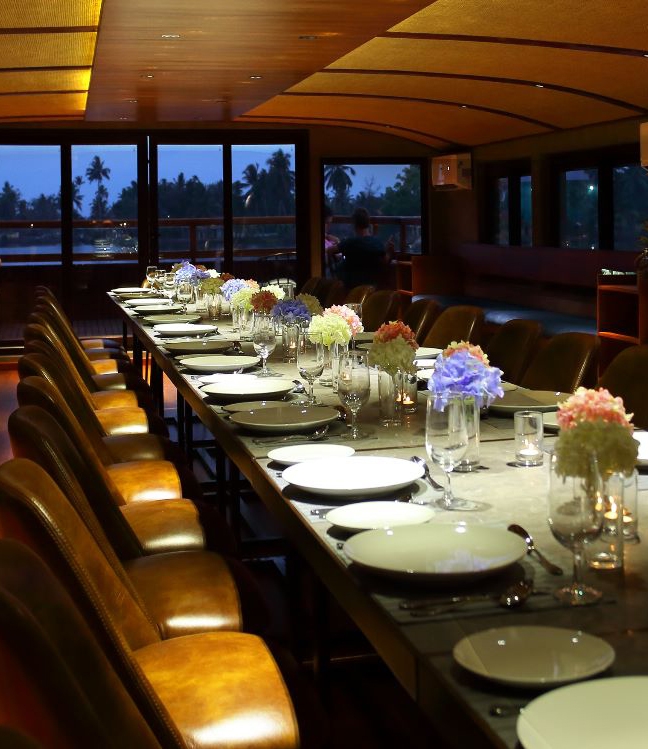 Elegant dining setup with floral centerpieces, plates, and dim lighting, overlooking palm trees.