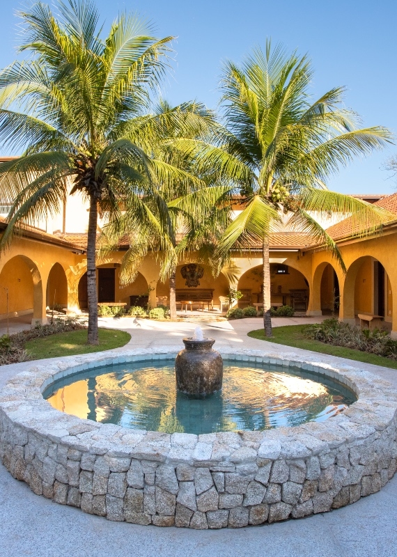Courtyard with fountain, palm trees, and archways in a sunny villa.