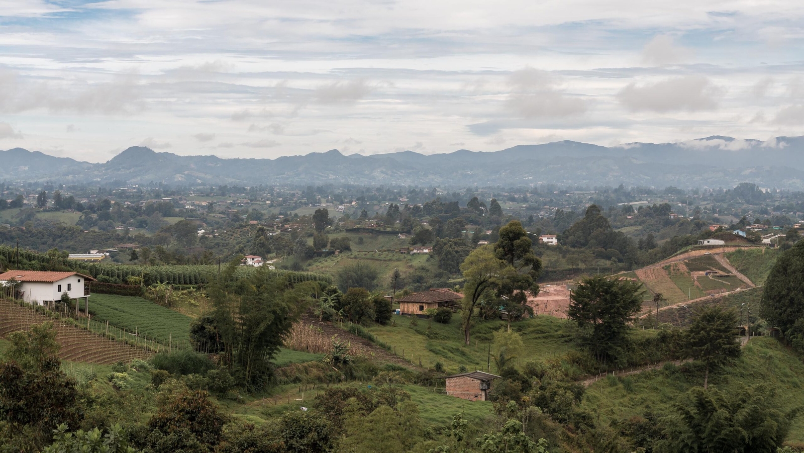Lush green Colombian landscape with farmland, mountains, and cloudy skies.