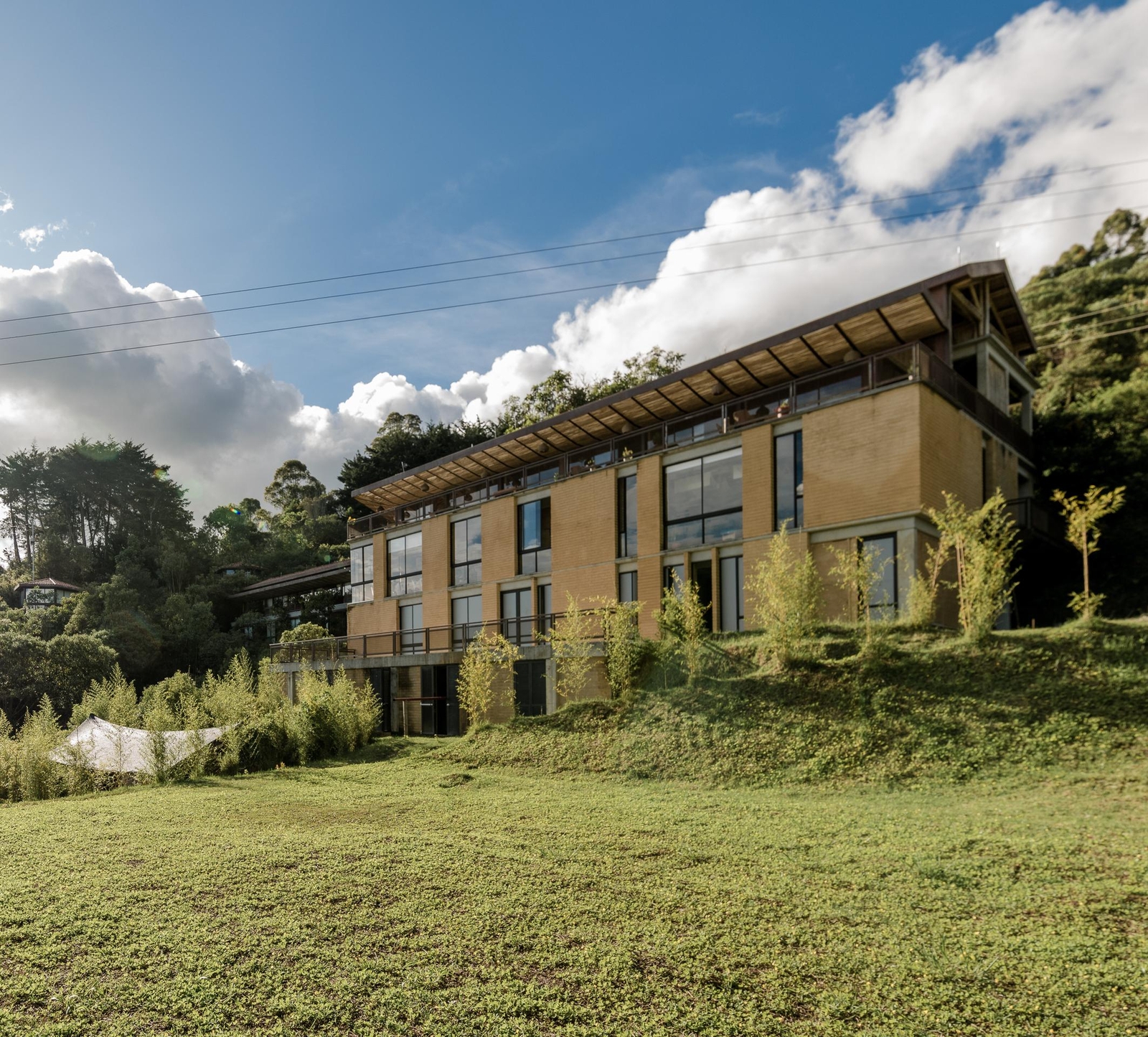 Modern multi-story building with large windows amidst lush greenery under a blue sky with clouds.
