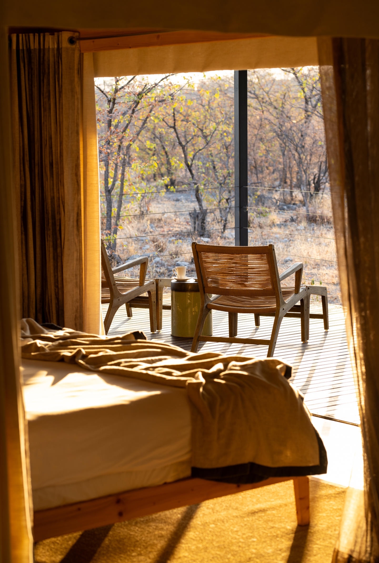 A cozy bedroom with a warm light, looking out onto an autumnal landscape through a glass door.