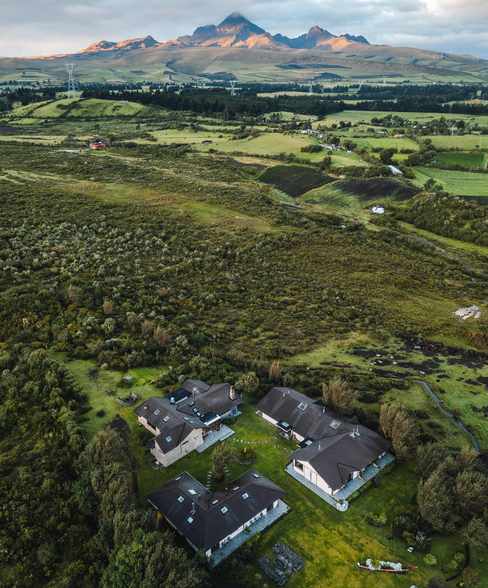 Aerial view of rural landscape with houses, green fields, and distant mountains at sunrise.