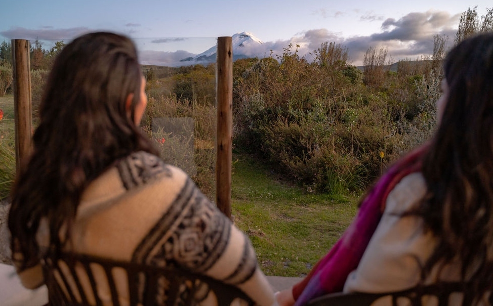 Two people gazing at a mountain landscape from a porch wrapped in blankets.