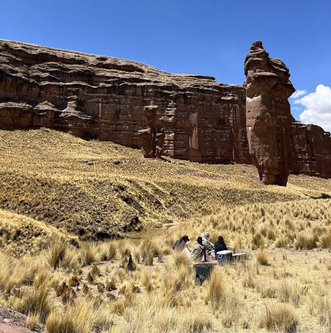 Several people resting on the ground beside a prominent rock formation, enjoying the scenic landscape.