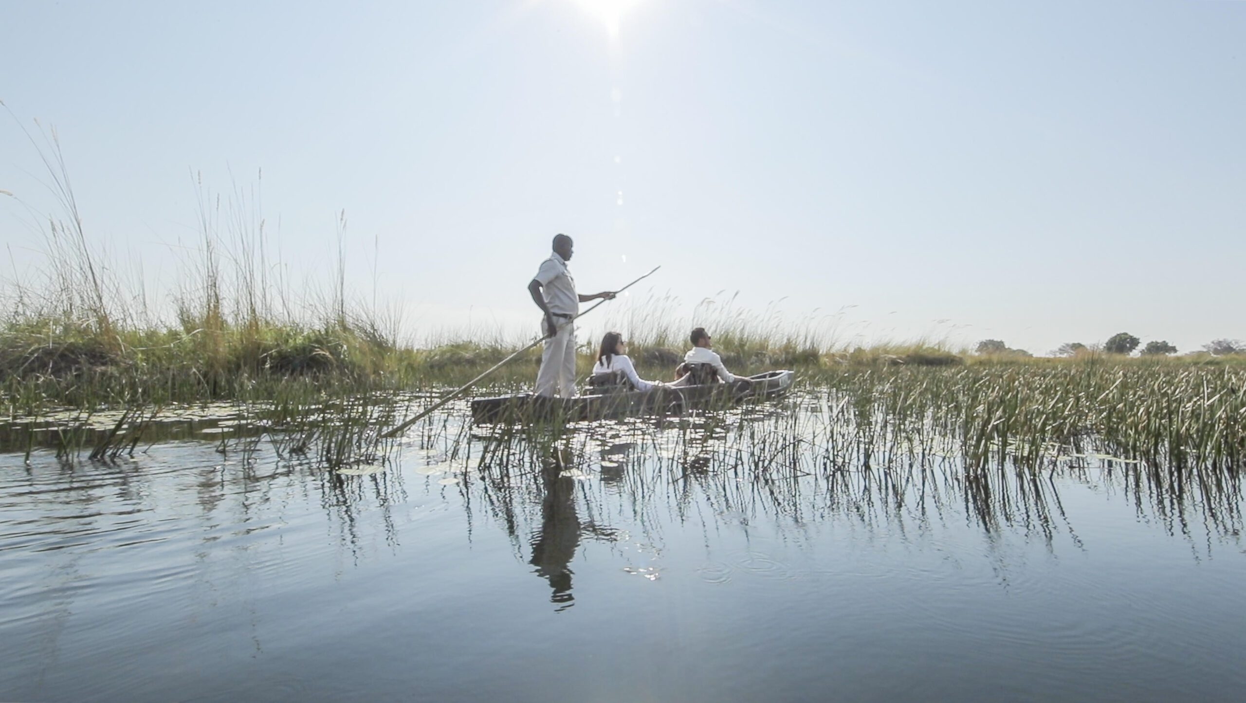 A couple gliding along a waterway on a traditional dugout canoe called a mokoro.