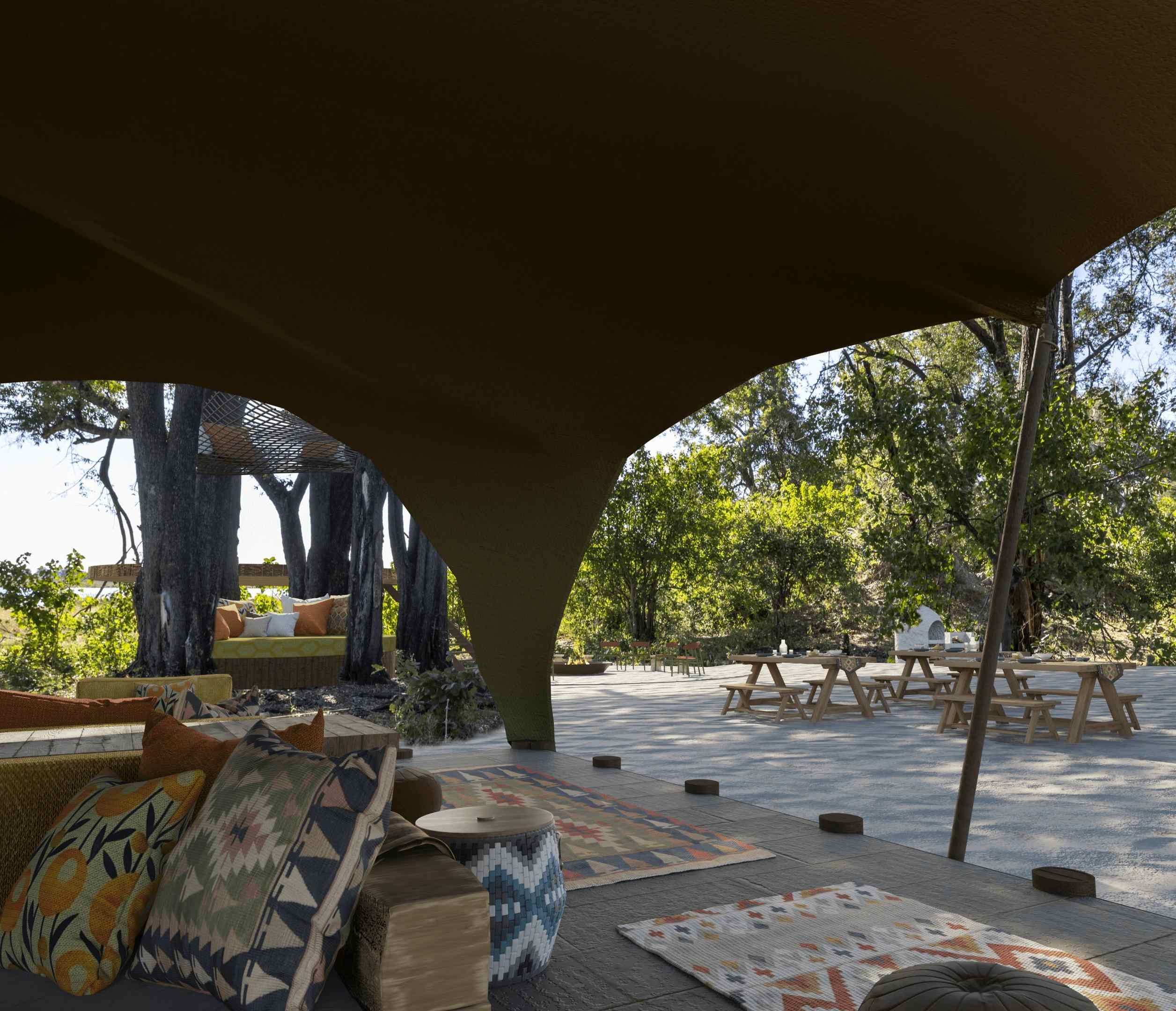 The communal area of Maxa Camp, featuring a cushioned lounging area beneath a canvas roof. There's also a courtyard with picnic style tables.