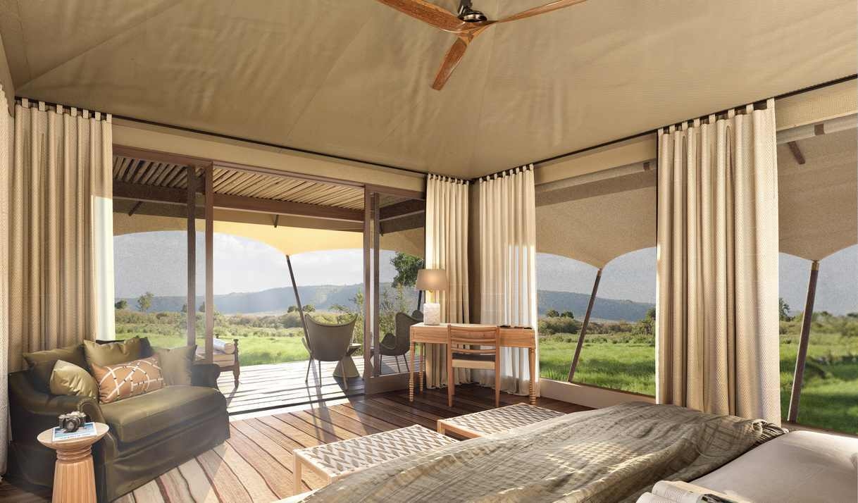 Interior of a luxury safari tent bedroom with wooden floors, neutral decor and a view of the grassy landscape..