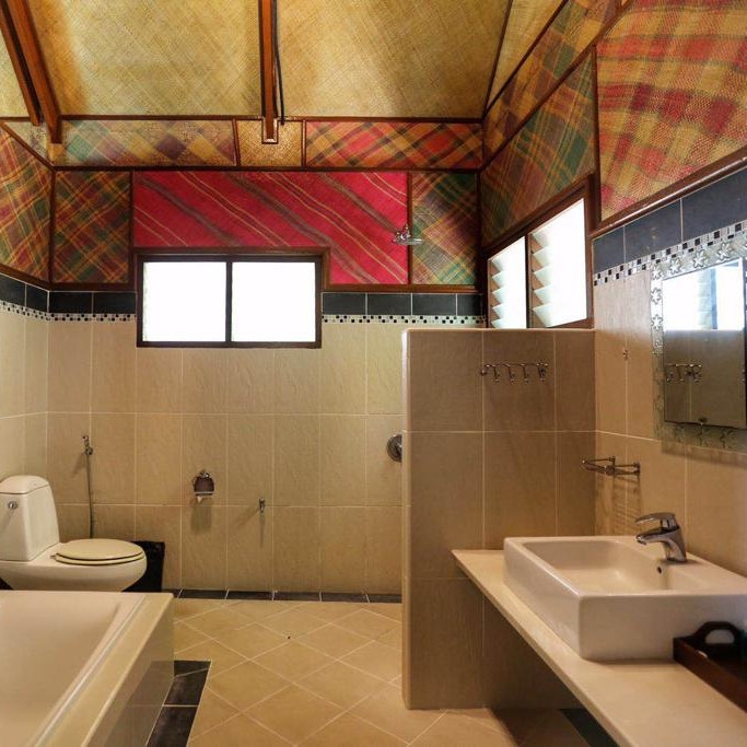 Interior of a bathroom with white tiled walls and colourful wallpaper on the upp half. There is a white bathtub, a toilet and a sink.