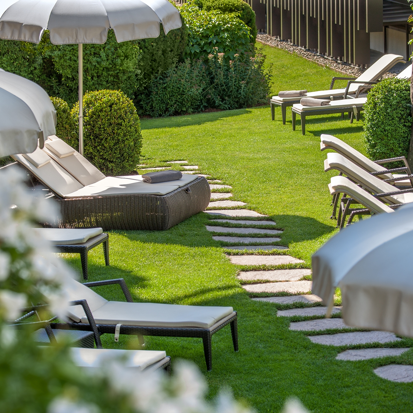 Lawn area with bright green grass, stone walkways and lounge chairs with white cushions and umbrellas.
