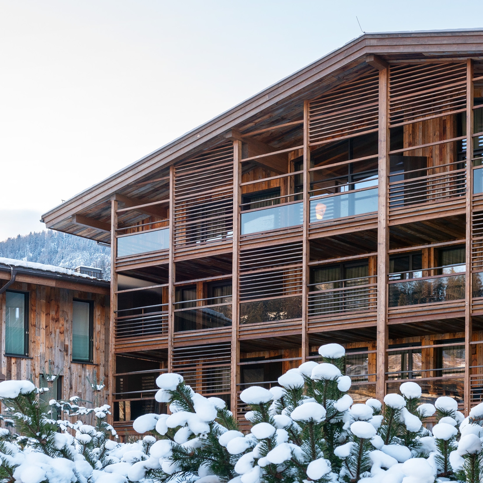 Exterior of the hotel's front with wooden balconies overlooking snow-covered pine trees.