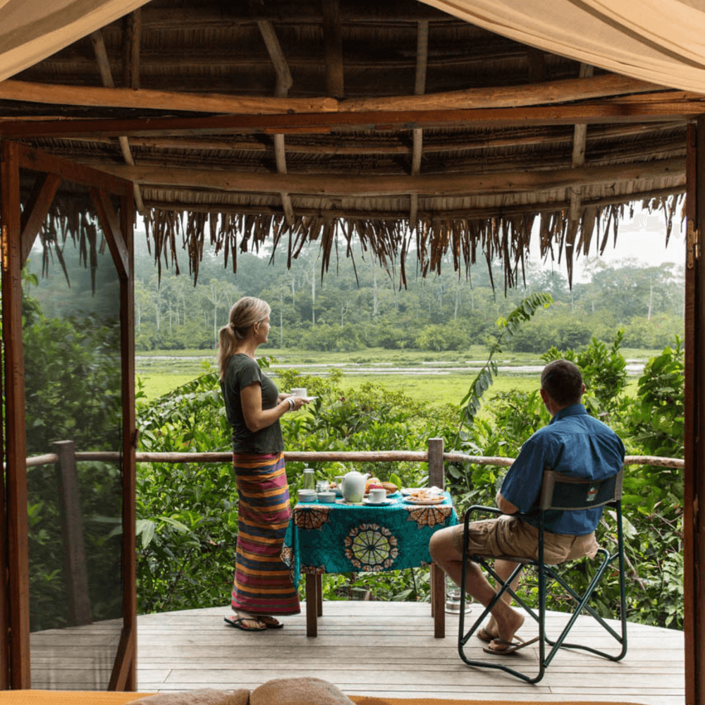 A couple looking out at the Lango baï from the deck of a thatched-roof bungalow