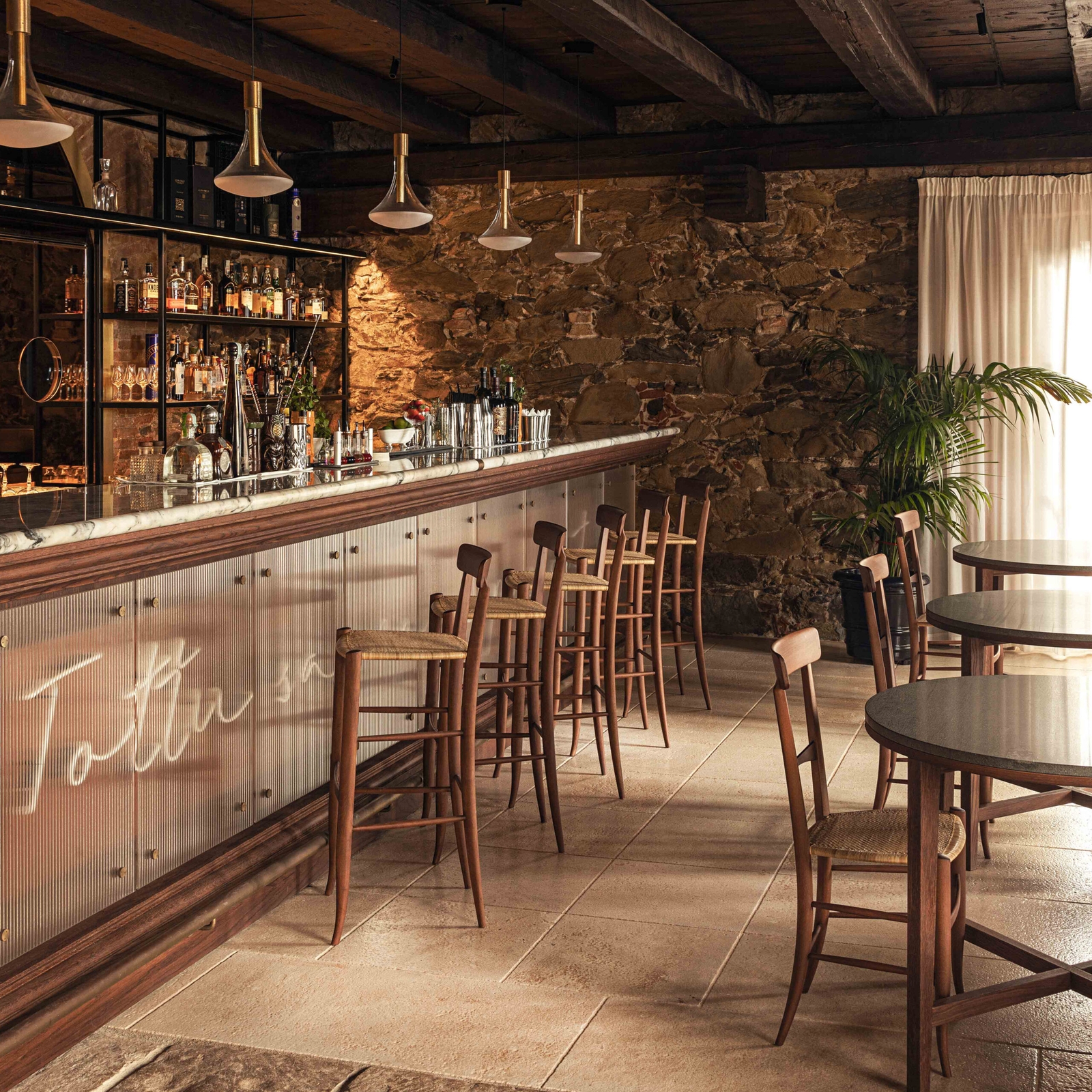 Interior of a bar with a long bar with high counter seating and a low lighting over the counter, plus a few tables and chairs.