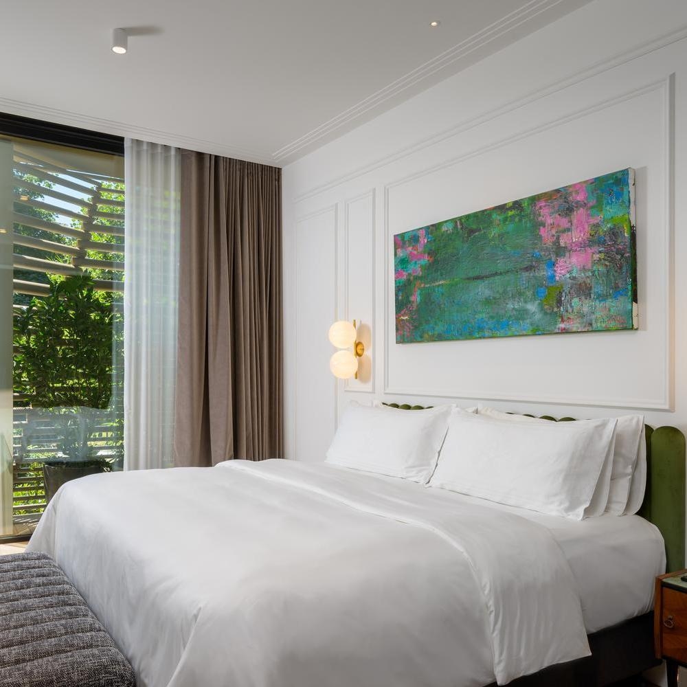 Bright hotel bedroom with white linens, a green headboard, and a large blue and green abstract painting.