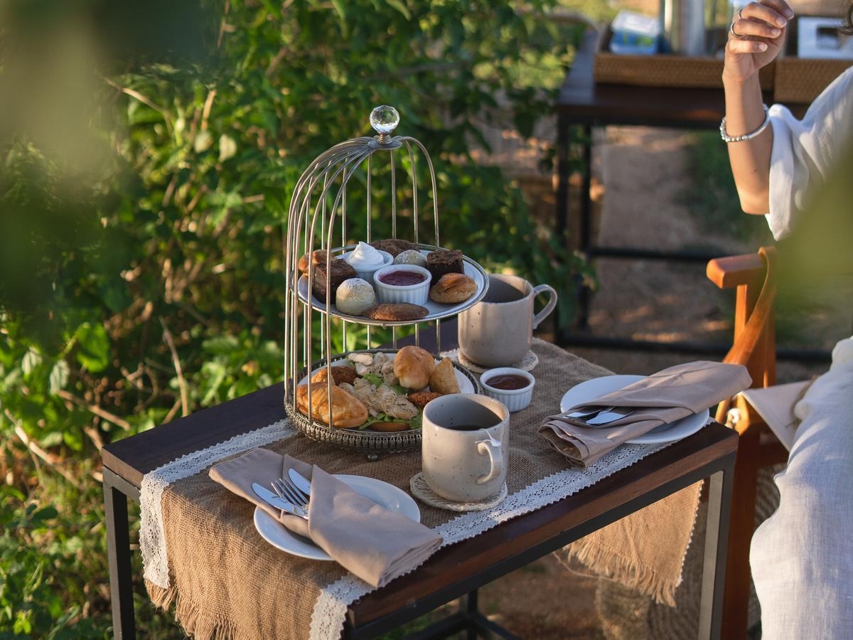 Afternoon tea stand with pastries and sandwiches on a small table next to ceramic mugs of tea.