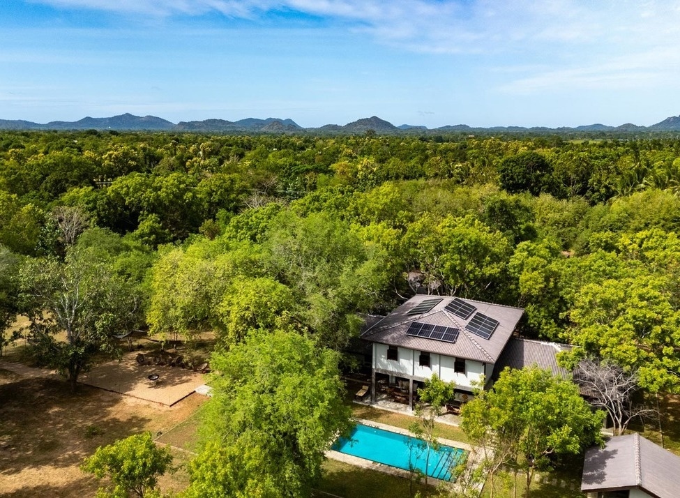 Aerial view of The Warden's House with a swimming pool and solar panels nestled in a lush green forest landscape.