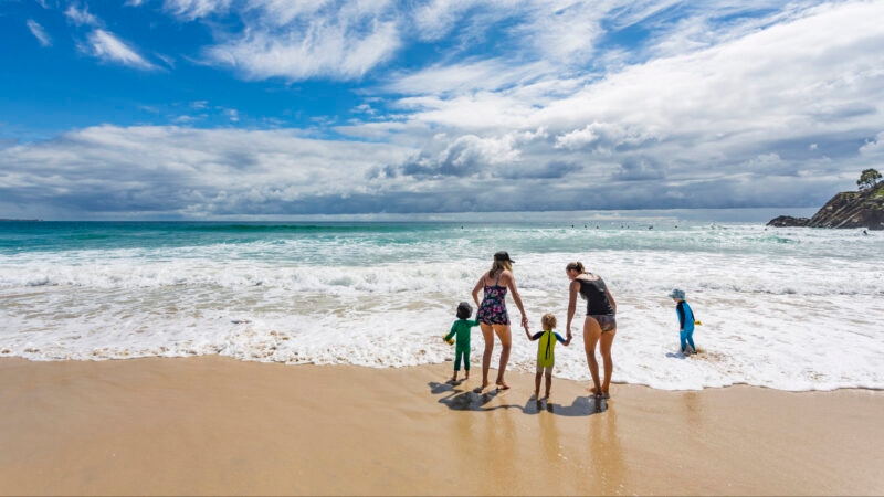 Group of mothers and children at the beach wearing sun protection clothes