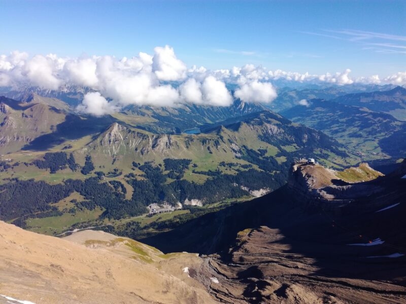 Aerial view of small grass-covered mountains and valleys in Switzerland with alpine lakes, and white fluffy clouds