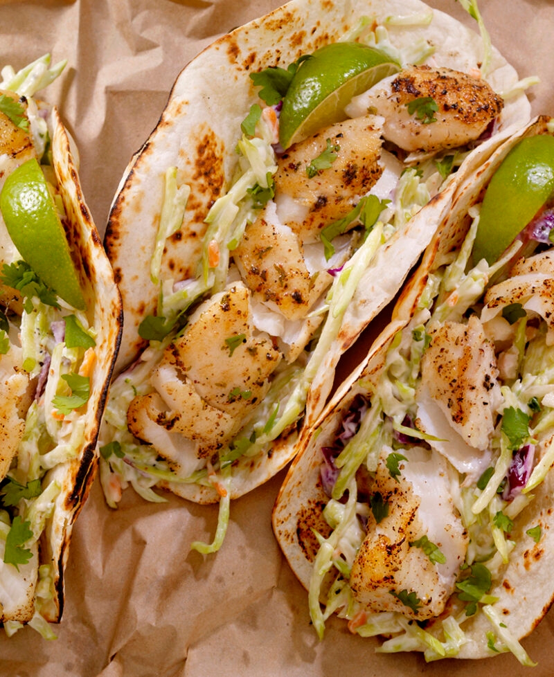 Three grilled fish tacos on flour tortillas with cabbage slaw, cilantro, and lime wedges, perfect for luxury Mexico tours.